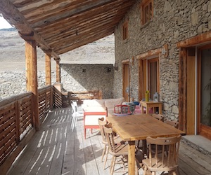 La grande terrasse couverte construite en bois massif du gîte Ancolie et les murs en pierres en plein été